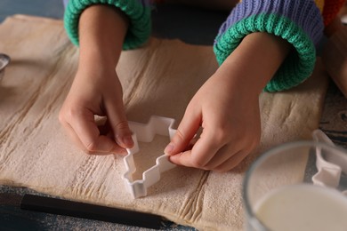 Photo of Little child cutting Christmas cookies at blue wooden table, closeup