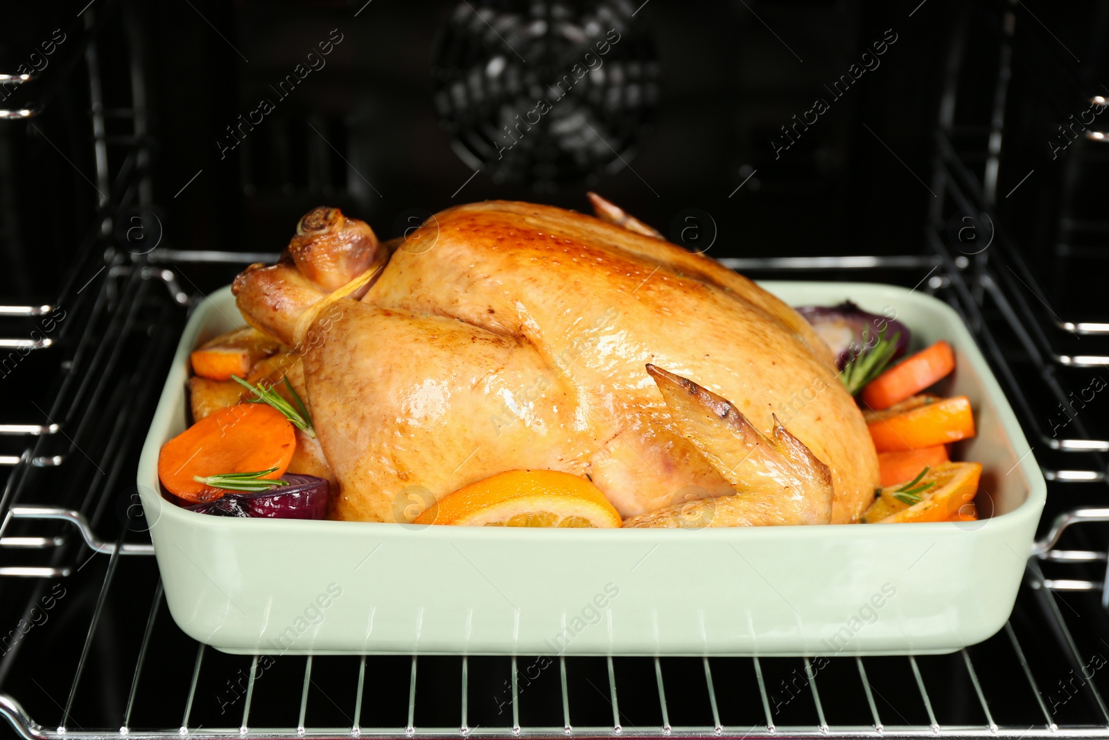 Photo of Baking pan with chicken, oranges and vegetables in oven