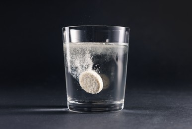 Photo of Effervescent pill dissolving in glass of water on grey table
