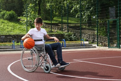 Photo of Disabled teenage boy in wheelchair playing basketball  on outdoor court