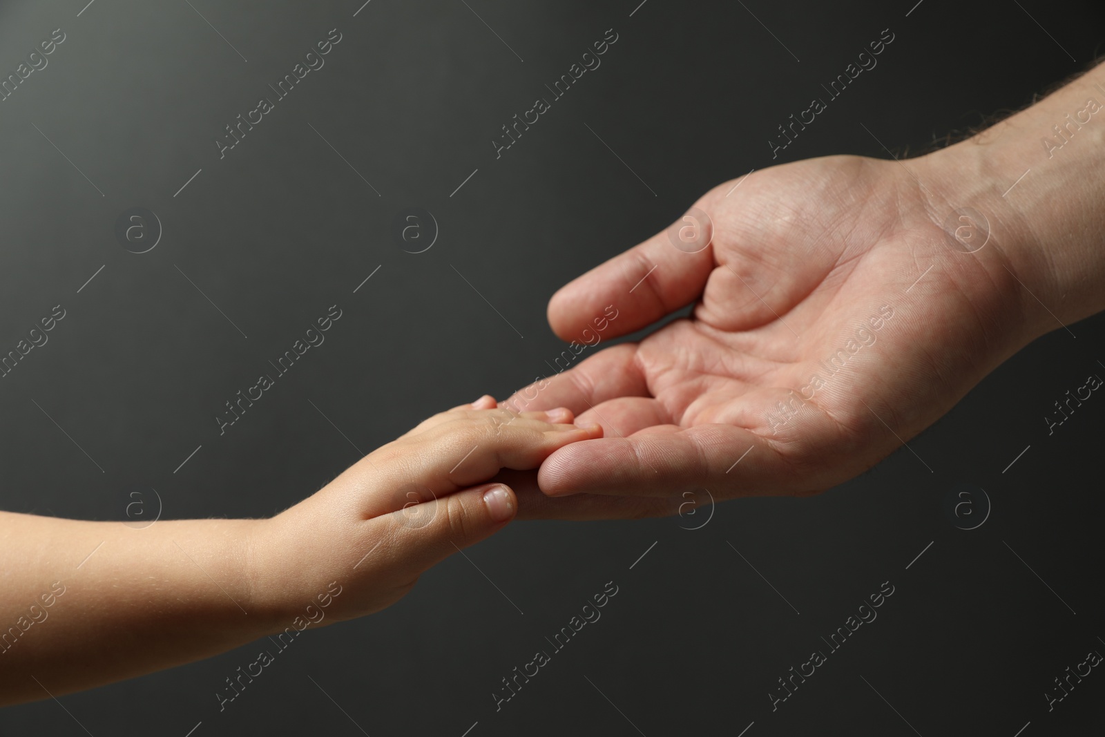 Photo of Father and child holding hands on dark grey background, closeup