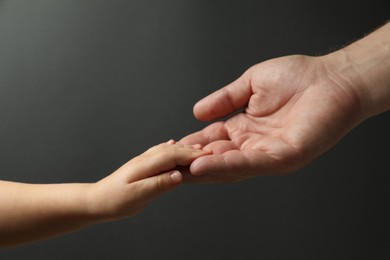 Photo of Father and child holding hands on dark grey background, closeup