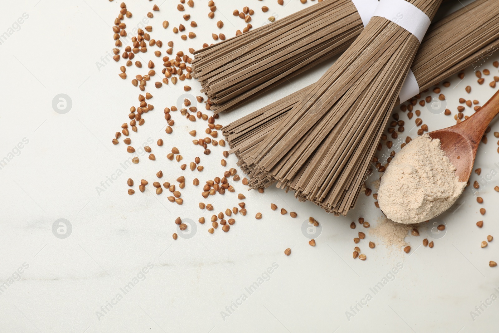 Photo of Uncooked buckwheat noodles (soba), flour and grains on white marble table, flat lay. Space for text