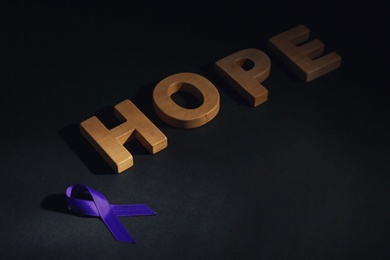 Purple awareness ribbon and word HOPE made of wooden letters on black background