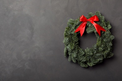 Photo of Christmas wreath made of fir tree branches with red ribbon on grey background, space for text