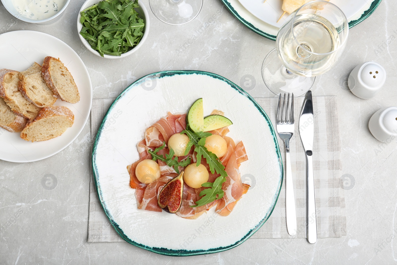 Photo of Flat lay composition with plate of melon balls and prosciutto on gray table