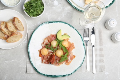 Photo of Flat lay composition with plate of melon balls and prosciutto on gray table