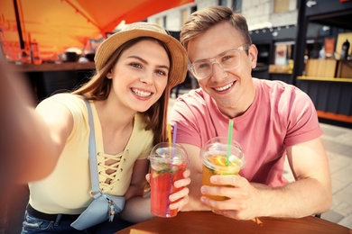 Photo of Young couple with summer drinks taking selfie in street cafe
