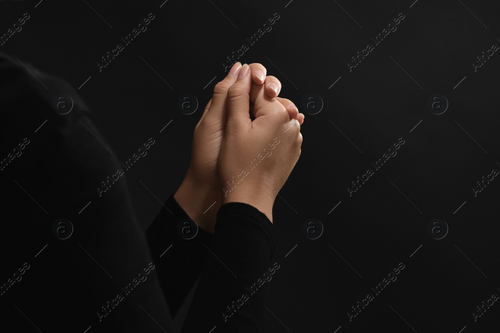 Photo of Woman holding hands clasped while praying against black background, closeup. Space for text