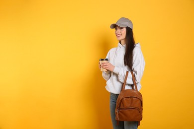 Photo of Beautiful young woman with stylish leather backpack and cup of coffee on yellow background. Space for text