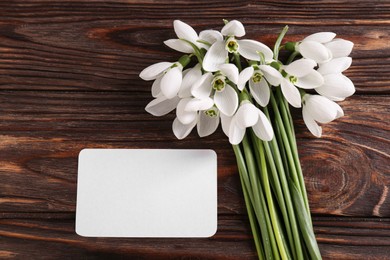 Photo of Beautiful snowdrops and paper card on wooden table, flat lay. Space for text