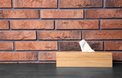 Photo of Napkin holder with paper serviettes on table against brick wall. Space for text