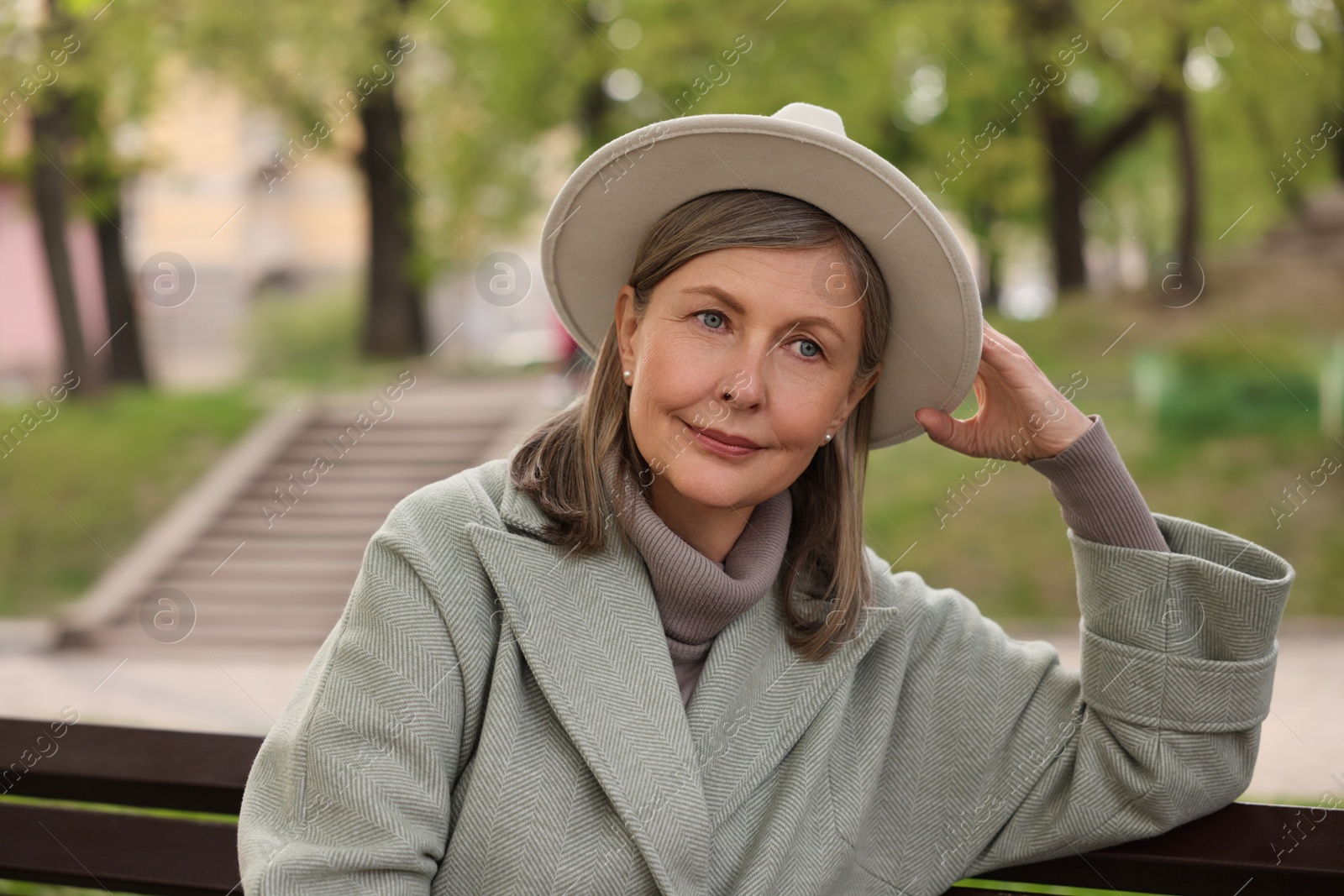 Photo of Beautiful senior woman sitting on bench outdoors, space for text