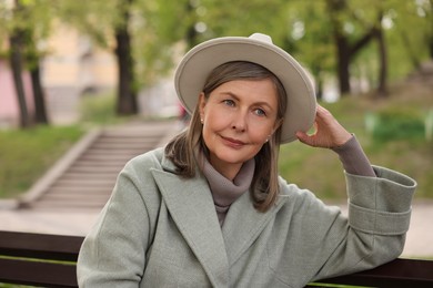 Photo of Beautiful senior woman sitting on bench outdoors, space for text