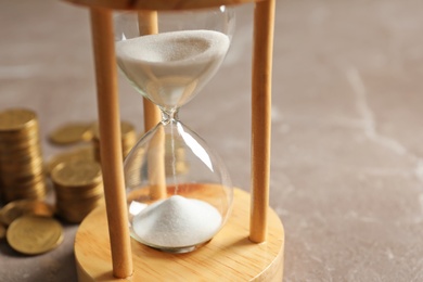 Hourglass with flowing sand and coins on table. Time management