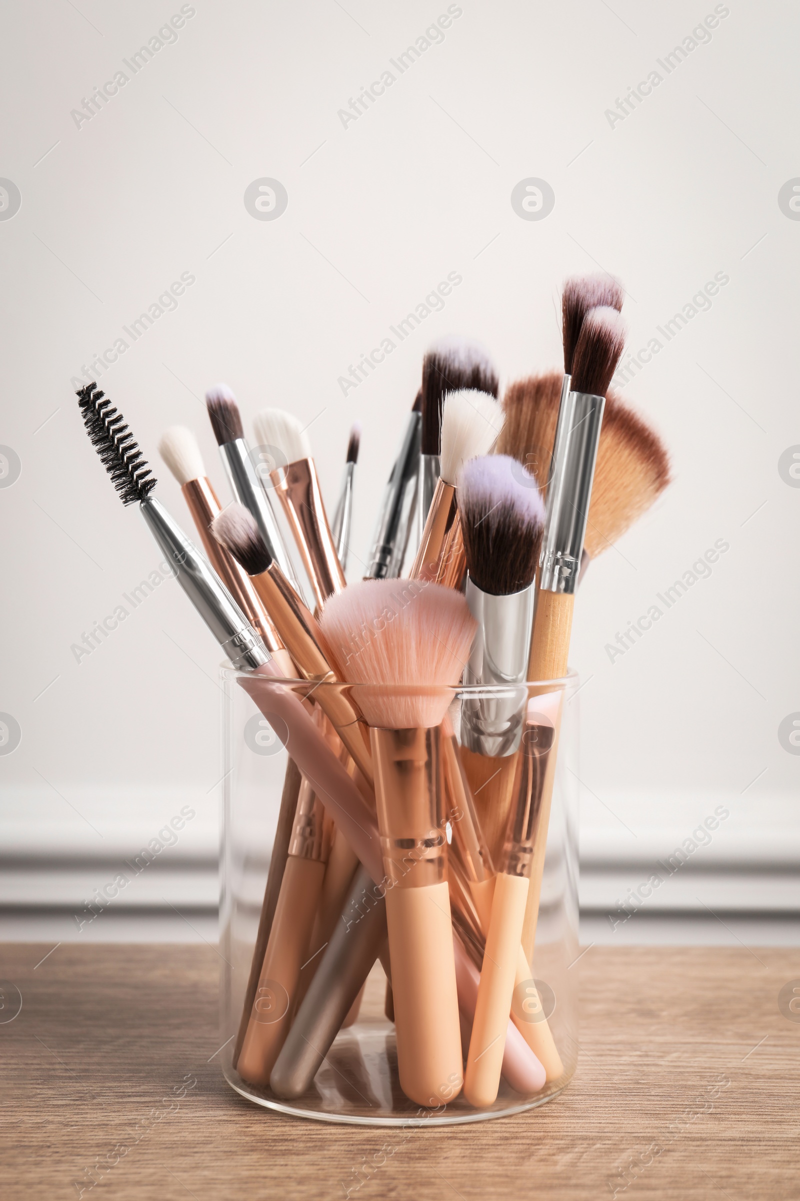 Photo of Set of professional makeup brushes on wooden table near white wall