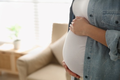 Pregnant woman touching her belly indoors, closeup