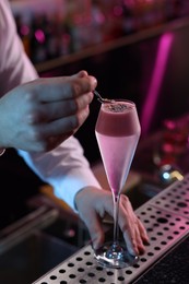 Photo of Bartender decorating fresh alcoholic cocktail with sprinkles at counter in bar, closeup