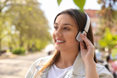 Photo of Young woman with headphones listening to music outdoors, space for text