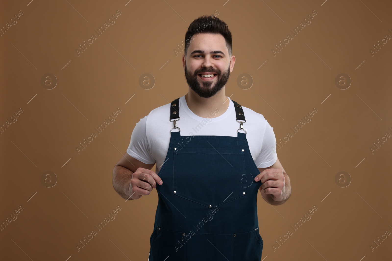 Photo of Smiling man in kitchen apron on brown background. Mockup for design