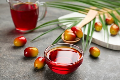 Photo of Palm oil in glass bowl, tropical leaf and fruits on grey table