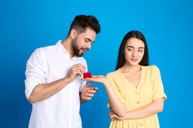 Photo of Young woman with engagement ring making marriage proposal of marriage to her boyfriend on blue background