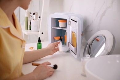 Woman taking cosmetic product out of mini refrigerator indoors, closeup