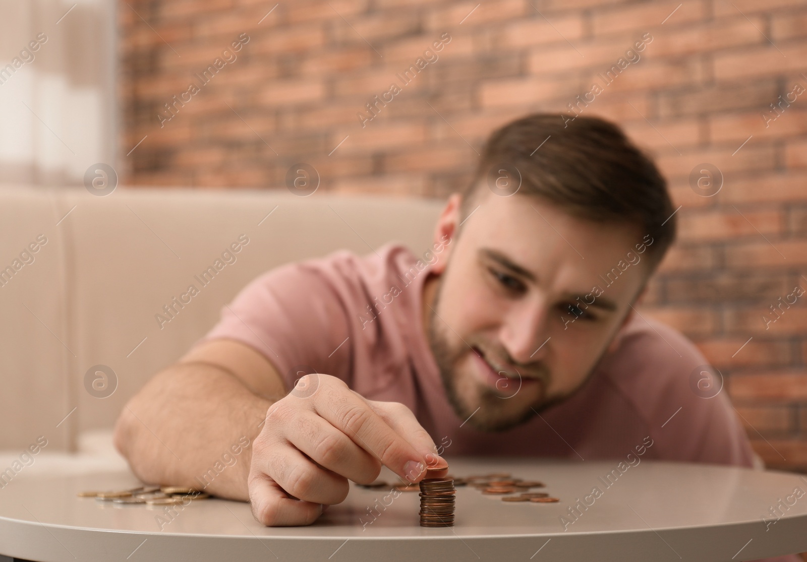 Photo of Young man with coins at home, closeup. Saving money