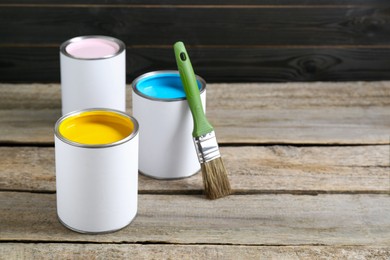 Cans of colorful paints with brush on wooden table, space for text