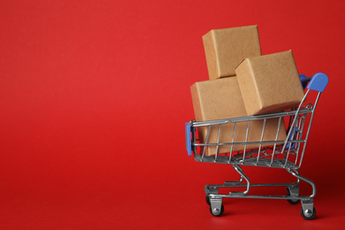 Photo of Shopping cart with boxes on red background, space for text. Logistics and wholesale concept