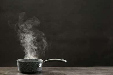 Photo of Steaming saucepan on grey table against dark background