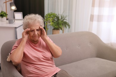 Photo of Senior woman with headache sitting on sofa at home. Space for text