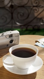 Photo of Cup of aromatic coffee and camera on wooden table outdoors