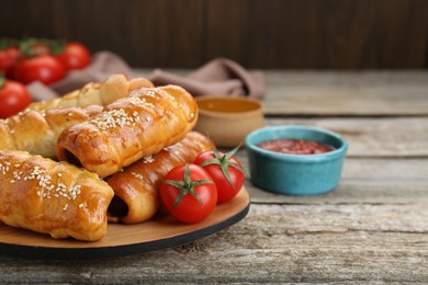 Delicious sausage rolls and ingredients on wooden table, closeup. Space for text