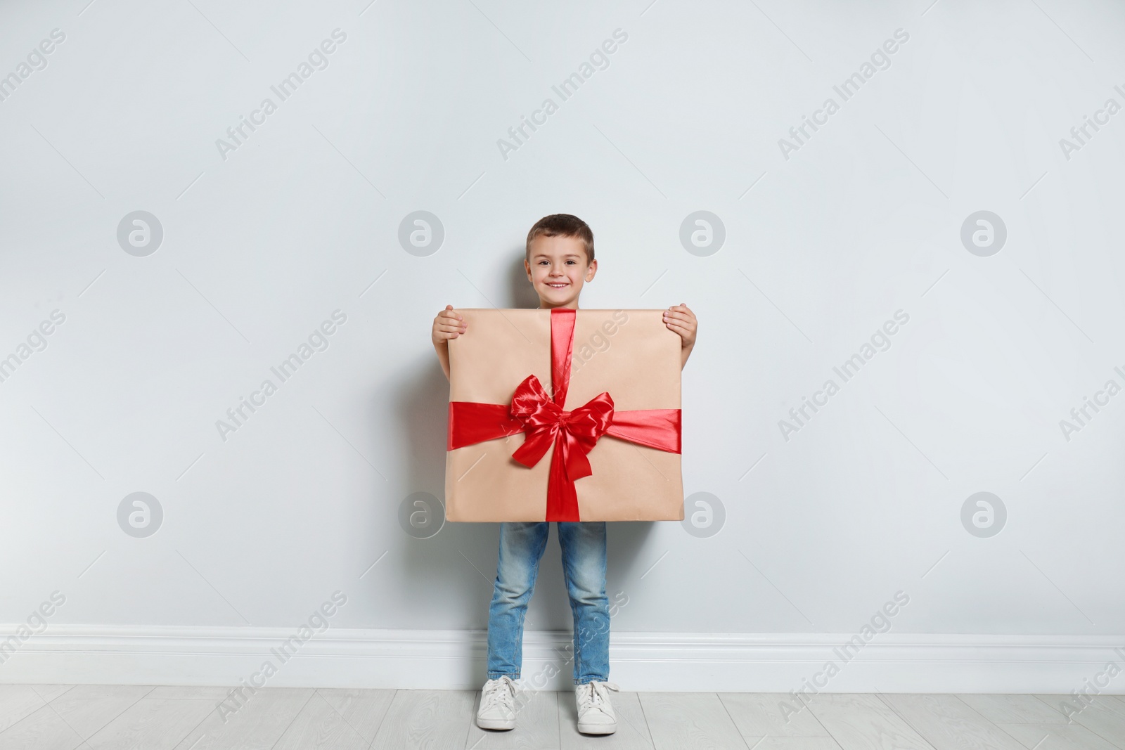 Image of Cute little boy dressed as gift box near white wall. Christmas suit