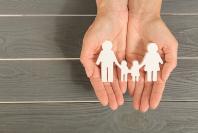 Woman holding figures of family in hands on grey wooden background, top view