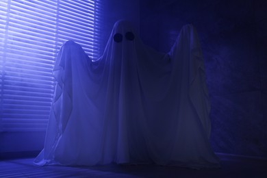 Photo of Creepy ghost. Woman covered with sheet near window in blue light