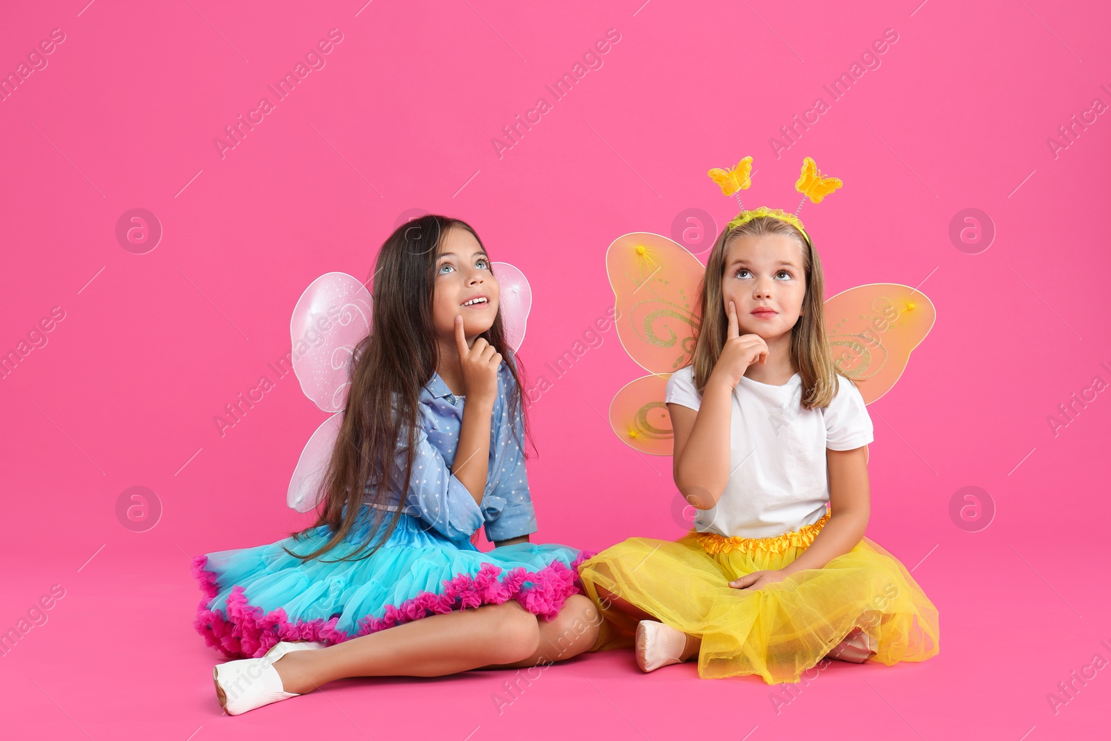 Photo of Cute little girls in fairy costumes with wings on pink background