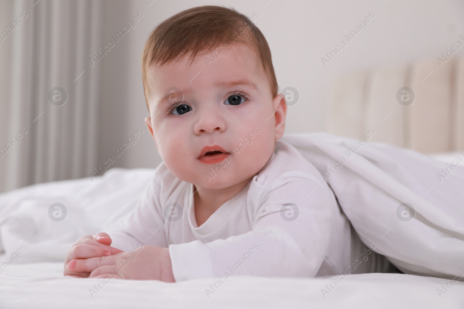 Photo of Cute little baby in bed under soft blanket indoors