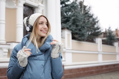 Photo of Young woman with headphones listening to music outdoors. Space for text