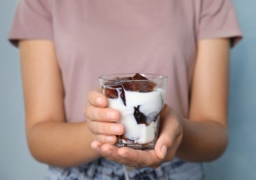 Photo of Woman holding glass of milk with delicious grass jelly on light blue background, closeup