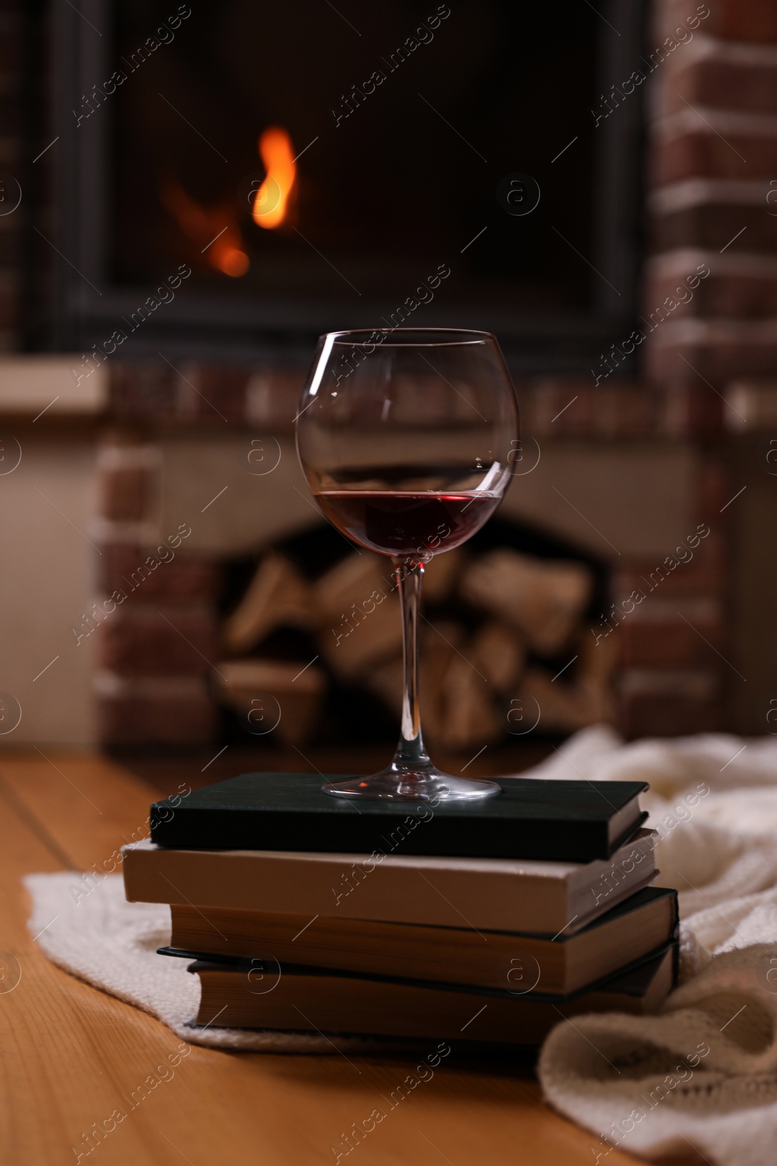 Photo of Glass of wine on books near fireplace indoors