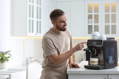 Photo of Young man preparing fresh aromatic coffee with modern machine in kitchen