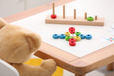 Photo of Stacking and counting game on table and teddy bear indoors, closeup. Educational toy for motor skills development