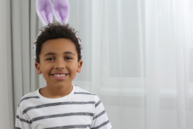 Photo of Cute African American boy with Easter bunny ears headband indoors, space for text