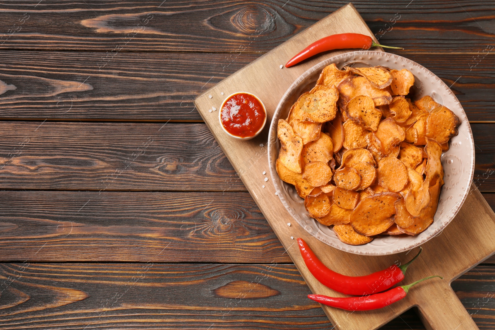 Photo of Board with plate of sweet potato chips, sauce and hot pepper on wooden table, top view. Space for text