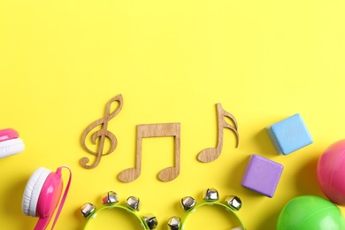 Photo of Baby song concept. Wooden notes, tambourines and toys on yellow background, flat lay. Space for text