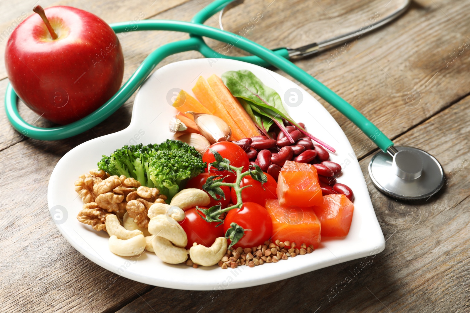 Photo of Plate with products for heart-healthy diet, apple and stethoscope on wooden background