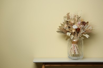 Beautiful dried flower bouquet in glass vase on white table near beige wall. Space for text