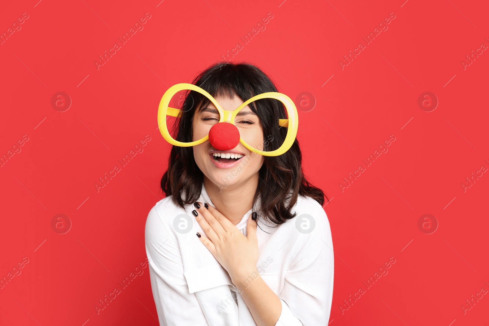 Photo of Joyful woman with large glasses and clown nose on red background. April fool's day